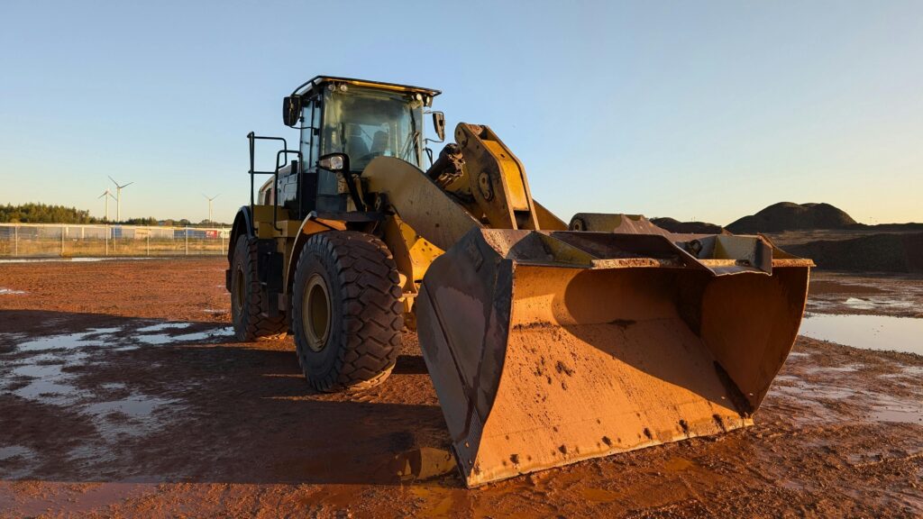 A large yellow bulldozer at a construction site during sunset, with wind turbines in the background.